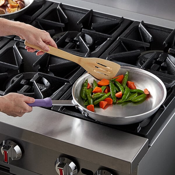 A person cooking vegetables in a Vollrath aluminum fry pan on a stove.