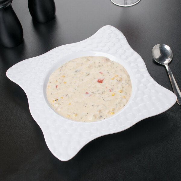 A white Las Brisas melamine bowl filled with soup on a white table.