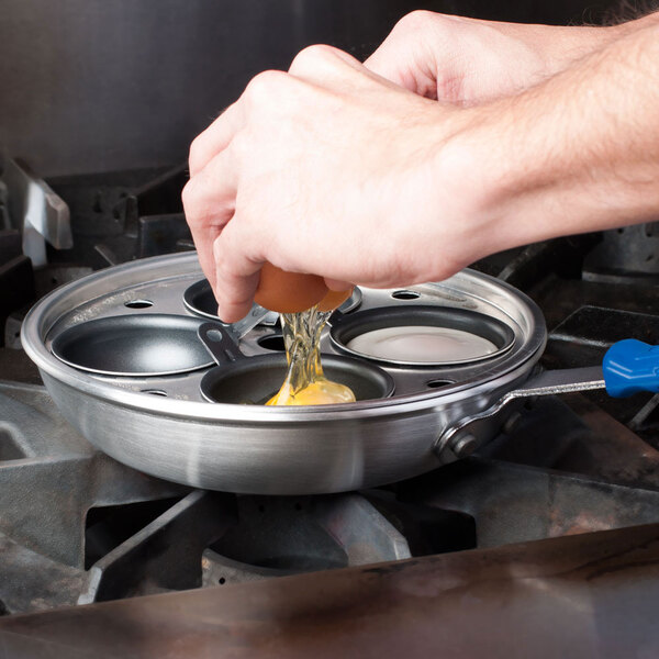 A person breaking an egg into a Vollrath Wear-Ever egg poacher cup.