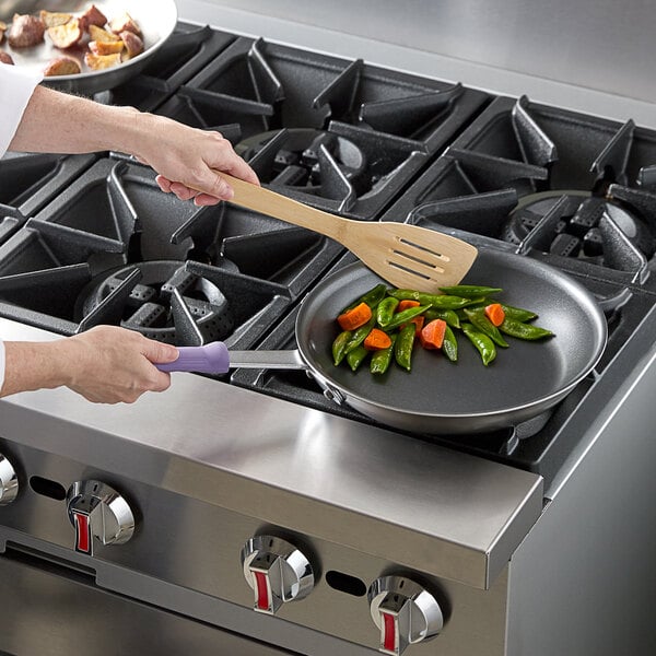 A person cooking vegetables in a Vollrath stainless steel fry pan.