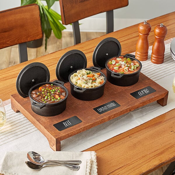 A rustic chestnut display stand with three cast iron pots of food on a wood table.