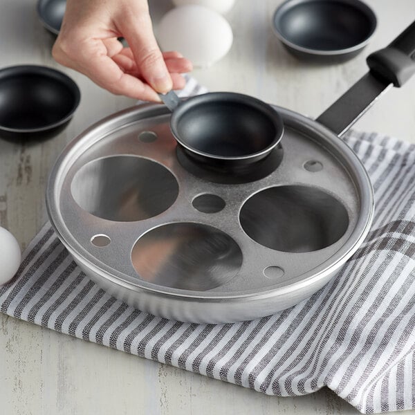 A woman using a Vollrath aluminum egg poacher inset on a pan.