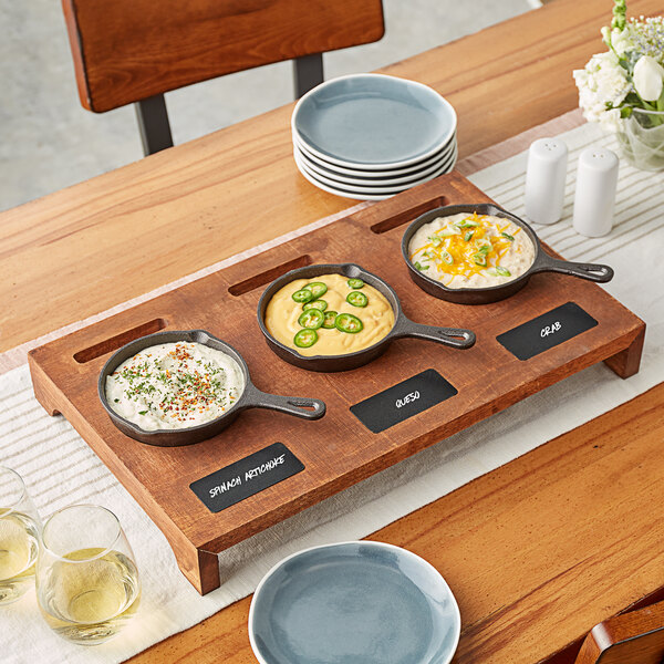 A rustic chestnut display stand holding three mini cast iron skillets filled with food.