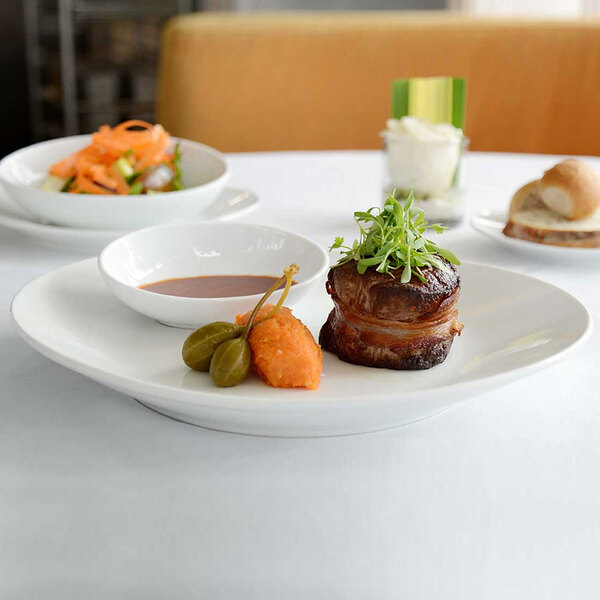 An Ellipse white porcelain oval coupe plate with a bacon wrapped steak and greens on top.