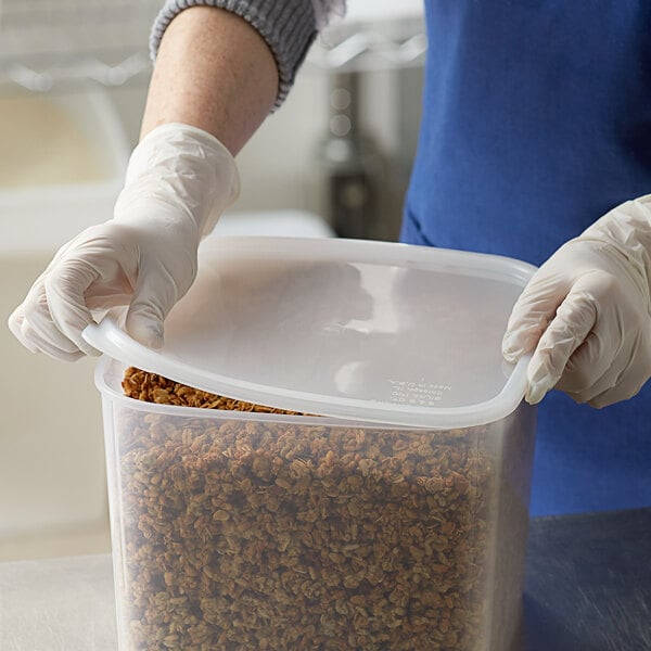 A person in a white coat holding a Carlisle translucent square plastic food container with food in it.