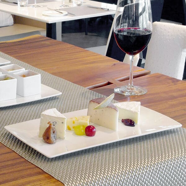 A white rectangular porcelain plate with cheese and fruit on a table.