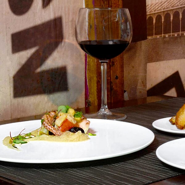 A white Front of the House porcelain plate with food on a table.