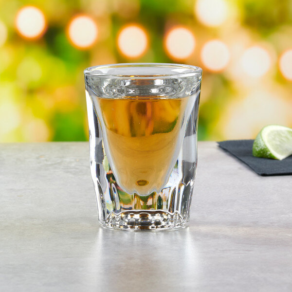 A clear fluted shot glass filled with a golden liquid, featuring a visible pour line.