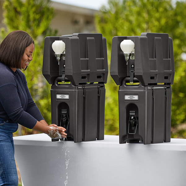 A woman using a black Cambro handwash station to wash her hands with soap.