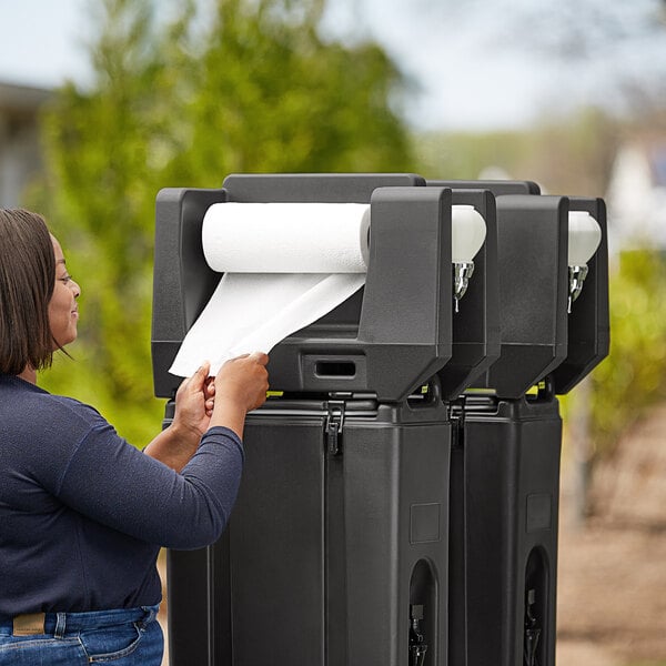 A woman using a black Cambro handwash station to dry her hands with paper towel.