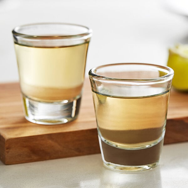 Two Anchor Hocking shot glasses on a cutting board.