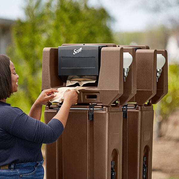 A woman putting a paper towel in a dark brown Cambro paper towel dispenser.