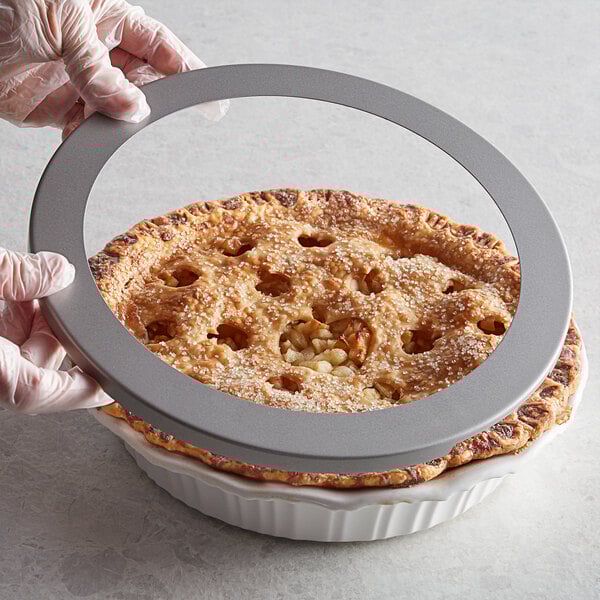 A person holding a pie with a Fox Run pie crust shield on a table.