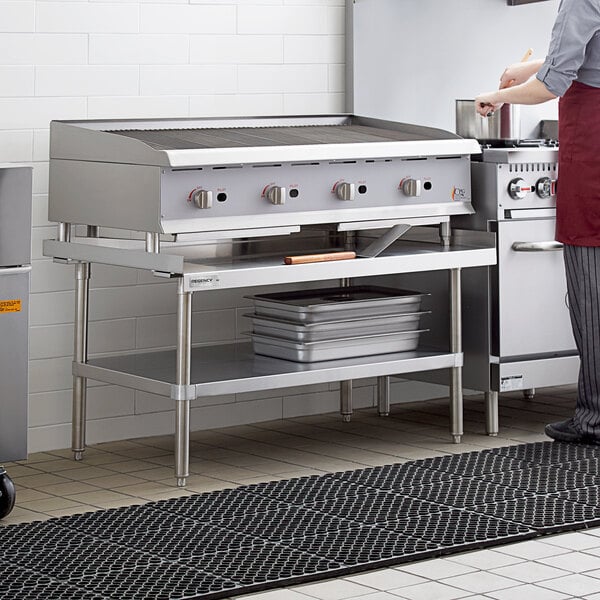 A woman standing in a professional kitchen next to a stainless steel Regency equipment stand.