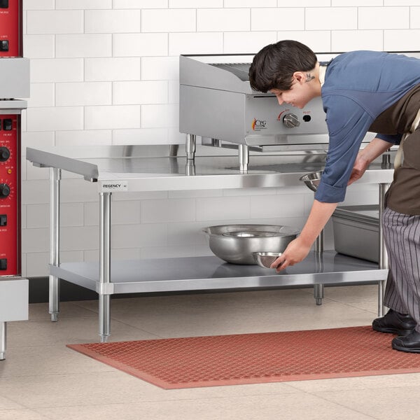 A man in a chef's uniform using a Regency stainless steel equipment stand in a school kitchen.