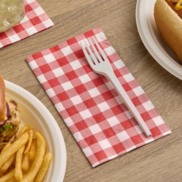 A red and white gingham 2-ply dinner napkin with a white plastic fork placed on top.