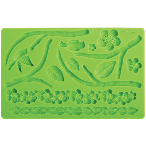 A green silicone Wilton mold with flowers, leaves, a bird, and a worm.