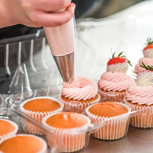 A hand using a pastry bag to put Rich's Bettercreme strawberry whipped icing on a cupcake.