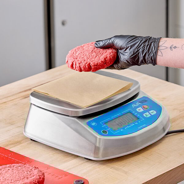 A hand in a black glove weighing a burger cutlet on an AvaWeigh digital scale.