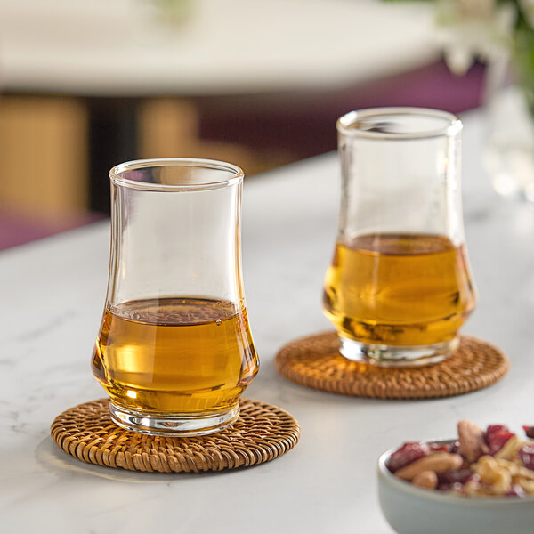 Two Arcoroc Kenzie whiskey taster glasses filled with brown liquid on a table in a cocktail bar.