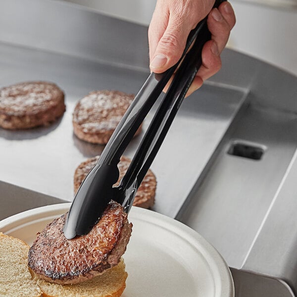 A person using Visions black disposable tongs to serve a burger.