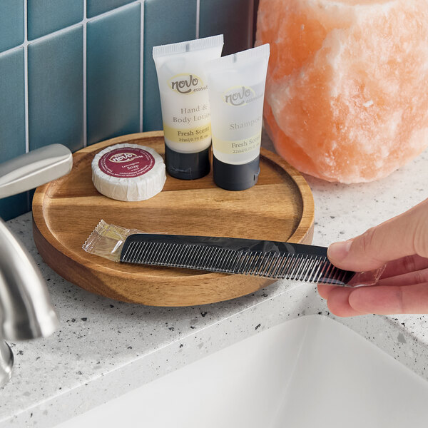 A black plastic comb individually wrapped in plastic, shown being picked up from a bathroom counter.