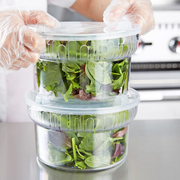 A person in gloves holding a Carlisle clear plastic crock filled with salad