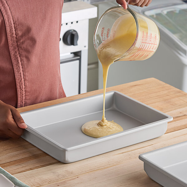 A rectangular anodized aluminum cake pan with straight sides being filled with batter.