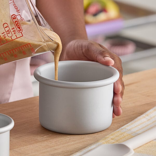 A small round anodized aluminum cake pan being filled with batter.