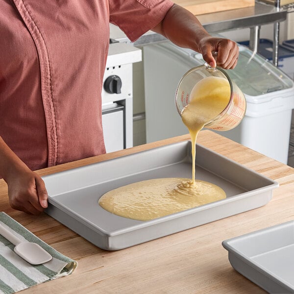 A rectangular anodized aluminum cake pan with straight sides being filled with batter.