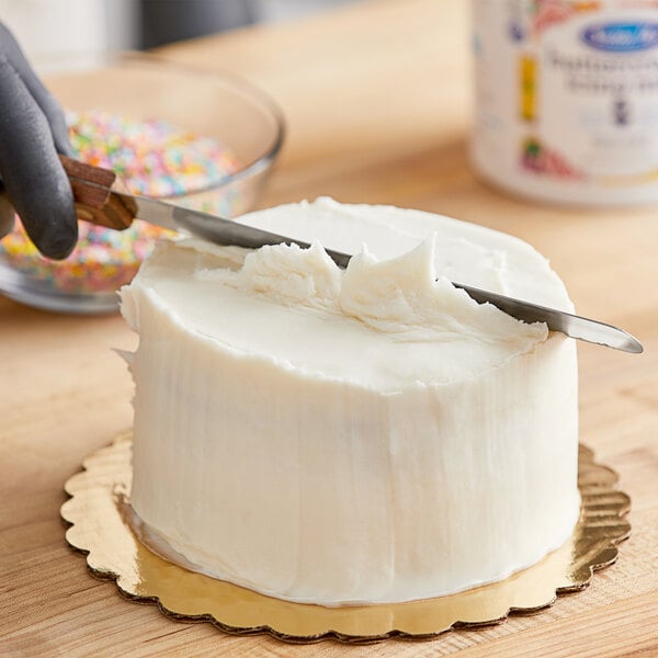 A person cutting a cake with Satin Ice white vanilla buttercream icing.