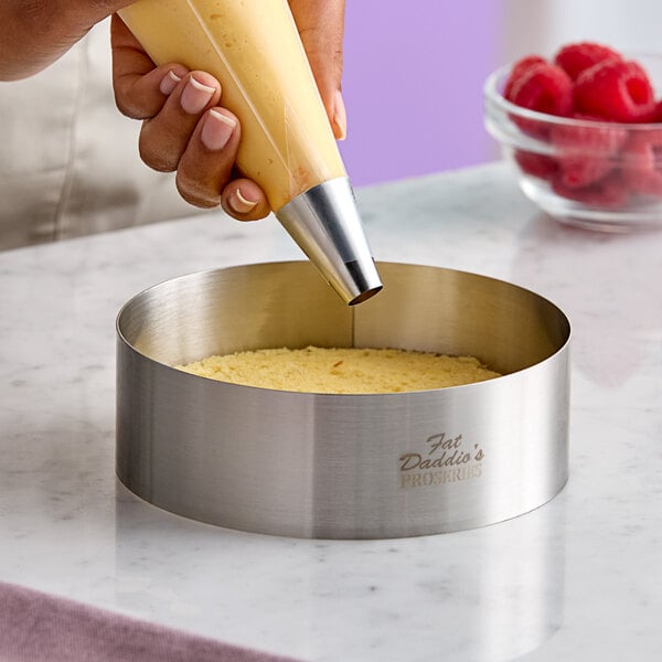 A stainless steel round cake ring being used to assemble a dessert.