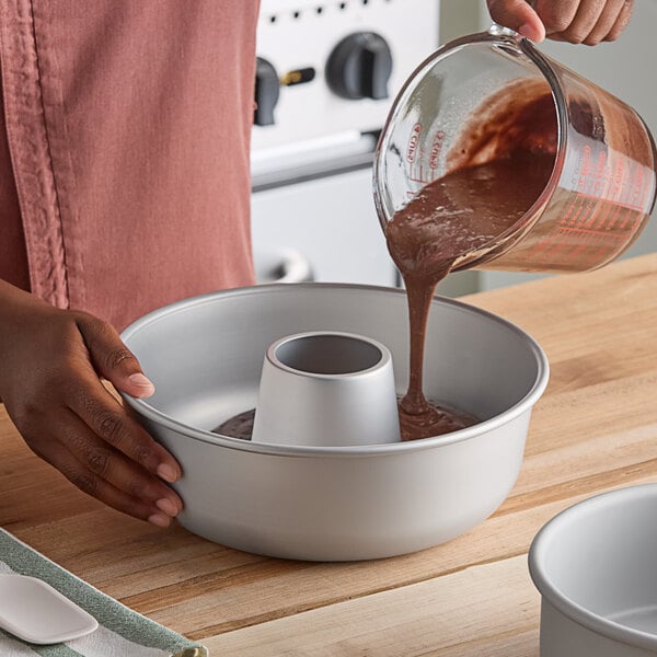 A person pouring cake batter into a Fat Daddio's ProSeries anodized aluminum ring cake pan on a wooden countertop.