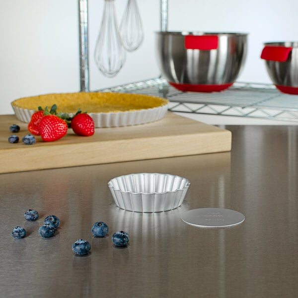 A Fat Daddio's round anodized aluminum fluted tartlet/quiche pan on a kitchen counter with a bowl of berries.