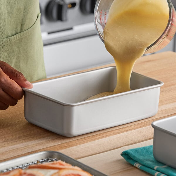 A rectangular anodized aluminum bread loaf pan being filled with batter.