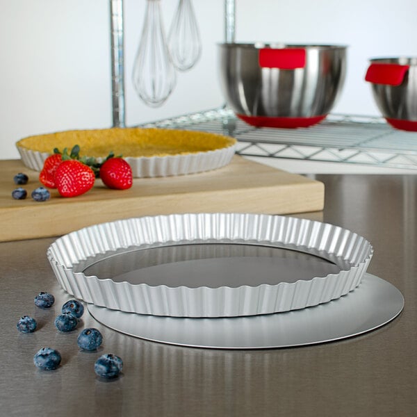 A Fat Daddio's round fluted tart pan on a counter with a bowl of strawberries.