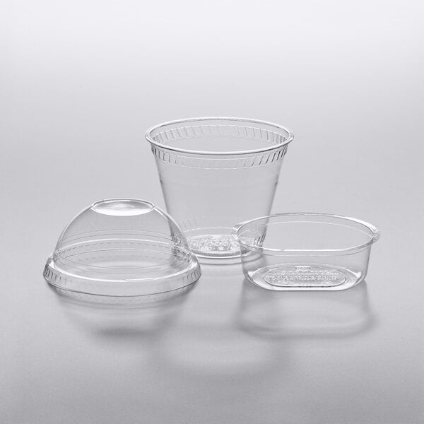 Fabri-Kal clear plastic parfait cups with dome lids on a gray surface.