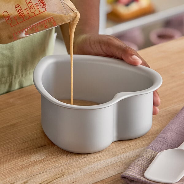 A heart-shaped anodized aluminum cake pan being filled with batter.