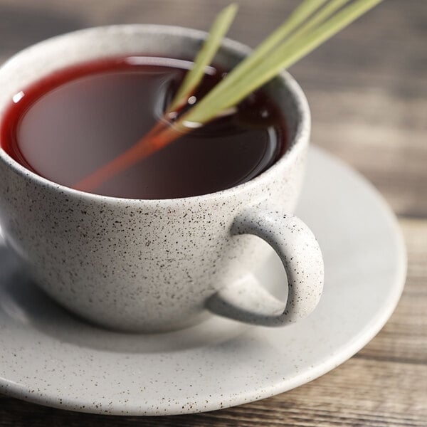 A saucer with a cup of tea with a sprig of rosemary on it.