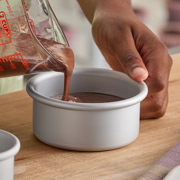 A small round anodized aluminum cheesecake pan with straight sides and a removable bottom being filled with chocolate batter.