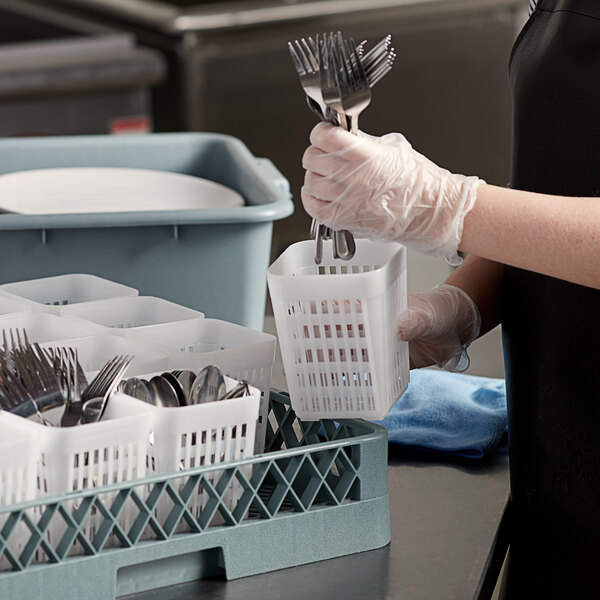 A person in a black apron holding a white plastic basket of silverware.