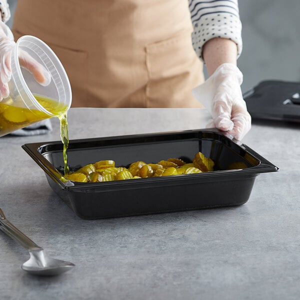 A hand pouring oil into a black Vigor plastic food pan.