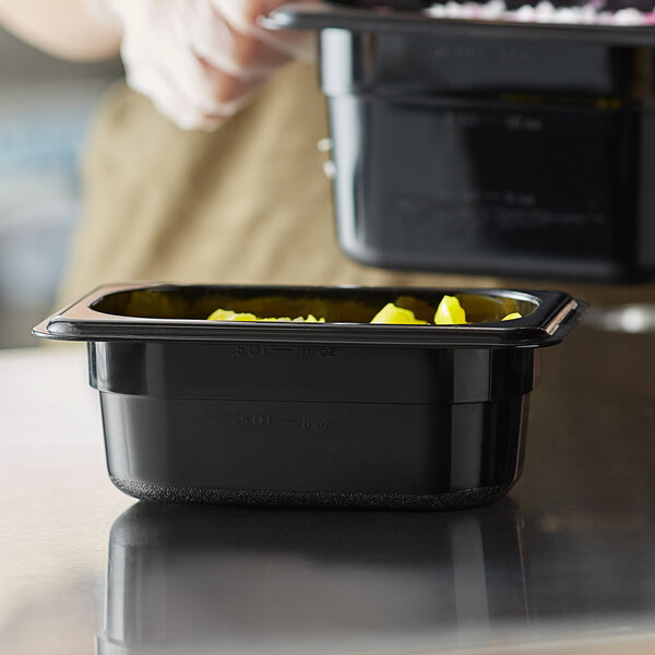 A person preparing food in a black Vigor polycarbonate food pan.