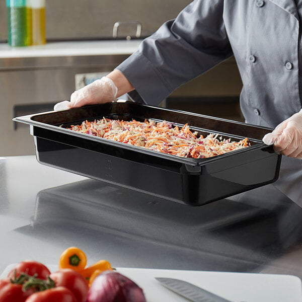 A chef holding a black Vigor food pan with vegetables.