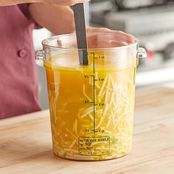 A person stirring food in a large clear container with green gradations.