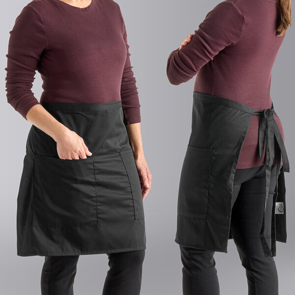 Two women wearing Mercer Culinary black bistro aprons standing at a kitchen counter.