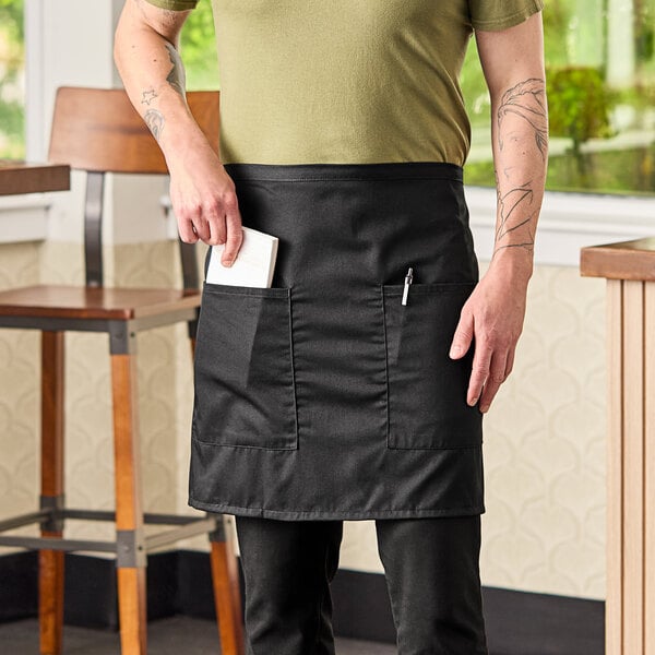 A man wearing a black Mercer Culinary short bistro apron with a pocket.
