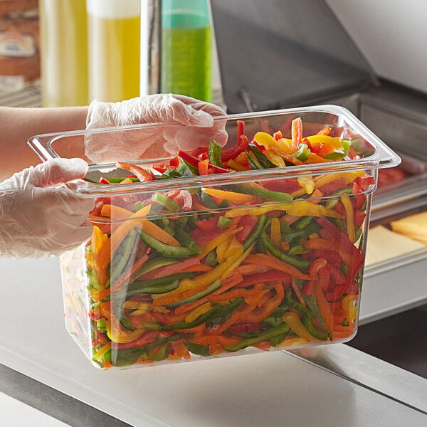 A person in gloves holding a Vigor clear polycarbonate food pan with food in it.