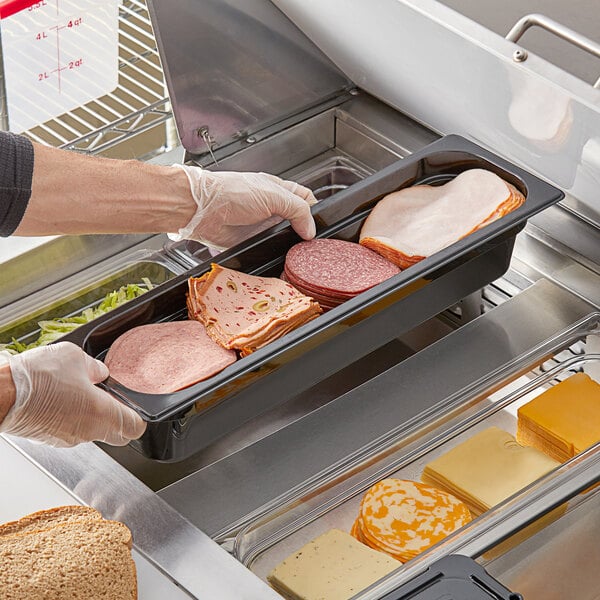 A person holding a Vigor black food pan filled with sliced meat on a counter.