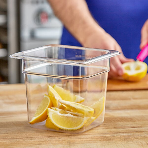 A hand squeezing lemon juice into a Vigor clear plastic food pan with lemon slices.